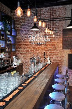 a bar with stools and lights hanging from the brick wall, along with several empty glasses