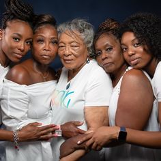 a group of women standing next to each other in front of a dark background with the woman's hands on her chest