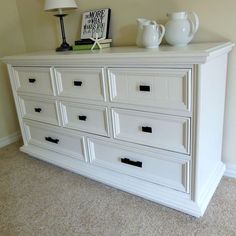 a white dresser sitting in a bedroom next to a lamp and pictures on the wall