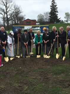 a group of people holding shovels standing next to each other on top of a field