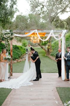 a bride and groom kissing under an outdoor wedding chute at the end of their ceremony