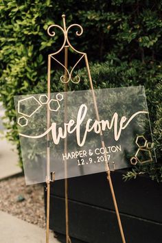 a welcome sign sitting on top of a wooden easel in front of a bush