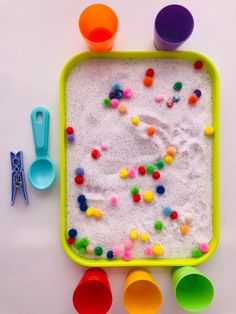 an assortment of colorful plastic bowls and spoons on a white surface with sprinkles