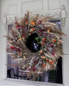 a wreath hanging on the front door of a house with dried flowers and leaves in it