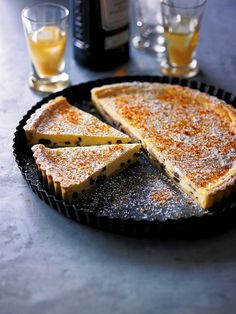 a pie sitting on top of a pan covered in powdered sugar next to two glasses