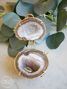 two agate shell pendants with gold chains on top of a marble table next to eucalyptus leaves