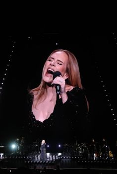 a woman singing into a microphone in front of a stage with lights and people on it