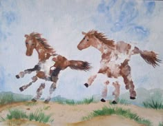 two horses running in the sand on a sunny day with blue sky and clouds behind them