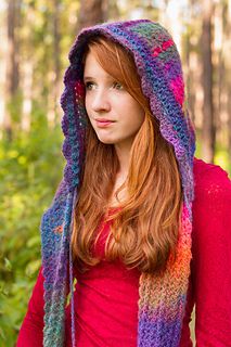 a woman with red hair wearing a purple and blue crochet hooded sweater in the woods