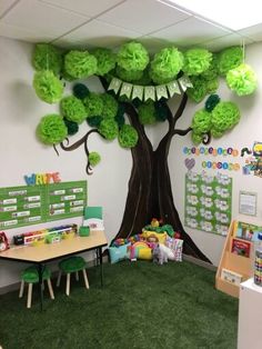 an office decorated in green and white with a tree on the wall, desks and children's toys