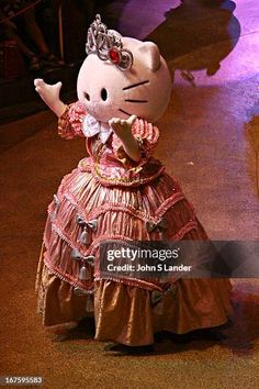 a hello kitty doll wearing a pink dress and tiara is standing in front of a stage