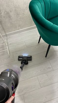 a person holding a camera in front of a green chair and a black object on the floor