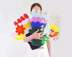 a woman is holding several colorful flowers in her arms and the other hand has an odd shaped object on it