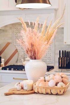 a white vase sitting on top of a counter next to a basket filled with eggs