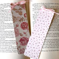 two bookmarks with pink flowers on them sitting next to an open book