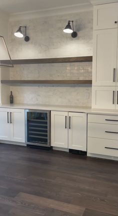 an empty kitchen with white cabinets and dark wood flooring is pictured in this image