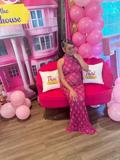 a woman sitting on a pink couch in front of a house with balloons and other decorations