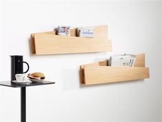 two wooden shelves holding books, magazines and a cup on a table next to each other