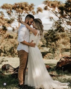 a man and woman standing in the grass with their arms around each other as they hug