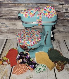 an old fashioned blue mixer with colorful cloths on the floor next to it's cover