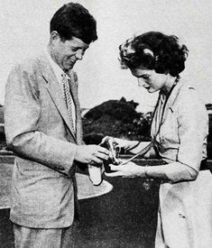 an old black and white photo of two people looking at something in their hands while standing next to each other