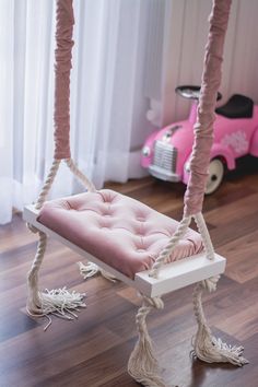 a pink car is parked next to a swing chair in the living room with white curtains