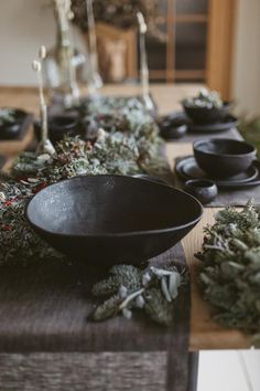 the table is set with black dishes and greenery