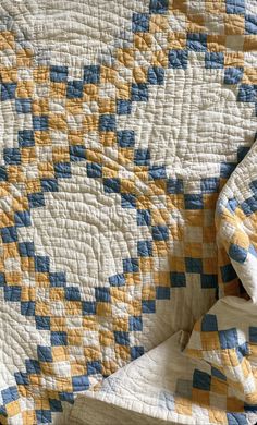 a bed with a yellow, blue and white quilt on it's coverlet