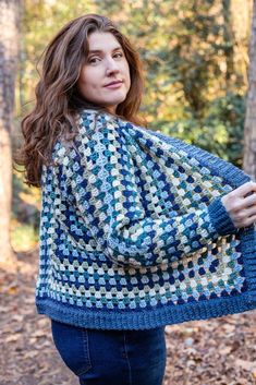 a woman standing in the woods wearing a blue and white crocheted shawl