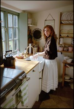 a woman standing in a kitchen next to a sink and stove with dishes on the counter