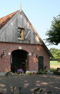 an old brick building with a wooden door and window on the front, surrounded by greenery