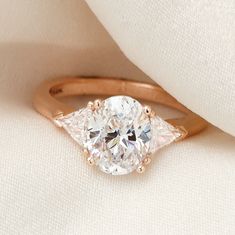 This lovely three-stone engagement ring features an oval diamond center framed by two trillion diamonds, creating the look of one large geometric diamond. JosephJewelry.com | Designed and created by Joseph Jewelry | Seattle, WA | Bellevue, WA | Online | Design Your Own Unique Engagement Ring | #engagementring Oval Rose Gold Ring For Anniversary, Fine Jewelry Three Stone Oval Ring, Fine Jewelry Three-stone Oval Ring, Rose Gold Oval Gemstone Rings, Timeless Oval Three Stone Ring, Three Stone Oval Cabochon Rings For Anniversary, Oval Rose Gold Diamond Ring With Gemstone, Oval Rose Gold Diamond Ring, Heirloom Oval Rose Gold Diamond Ring