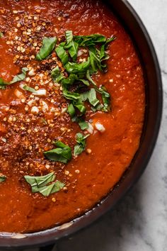 a pan filled with red sauce and garnish on top of a white table