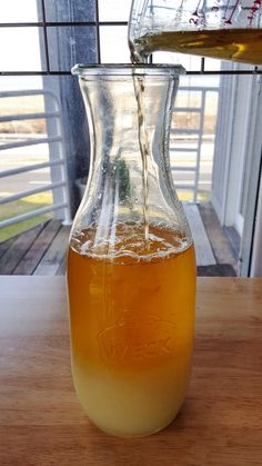 a pitcher filled with liquid sitting on top of a wooden table next to a window