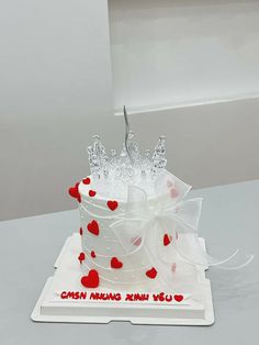 a white cake with red hearts and a tiara on top is sitting on a table