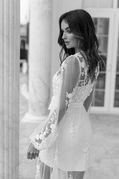 a woman standing in front of columns wearing a dress with flowers on the back and long sleeves