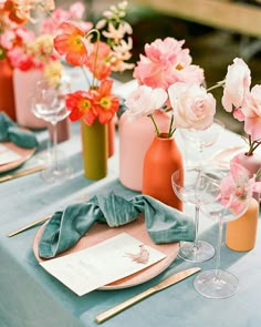 the table is set with pink and orange flowers in vases, napkins, and wine glasses