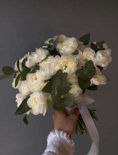 a person holding a bouquet of white roses and greenery in front of a gray background