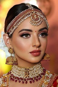 a woman in a red and gold bridal outfit with jewelry on her head, looking at the camera