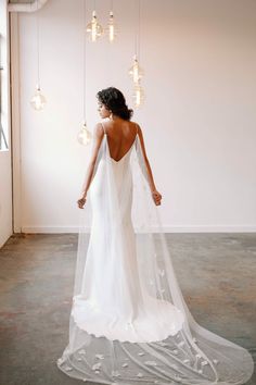 a woman in a white dress is standing with her back turned to the camera and wearing a long veil