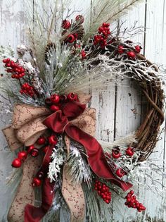 a christmas wreath with red berries and greenery hanging on a white wooden wall next to a door