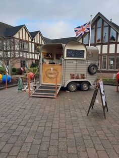 an old fashioned trailer is parked in front of a building with flags on the roof