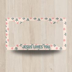 a white license plate with pink and blue flowers on it that says jesus loves you