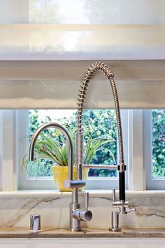 a kitchen sink and faucet in front of a window with potted plants