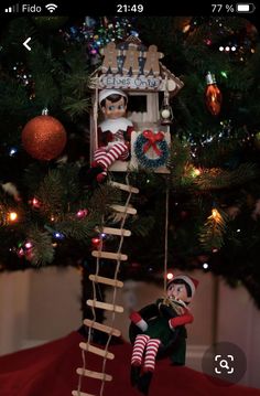 an elf is hanging from a ladder in front of a christmas tree