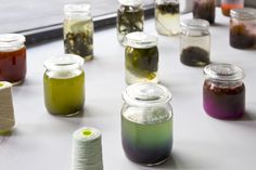 several jars filled with different colored dyes and spools of thread next to each other