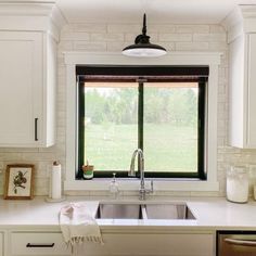 a kitchen sink under a window next to white cabinets