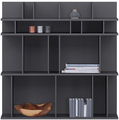 a book shelf with books, vase and other items on it in front of a gray wall