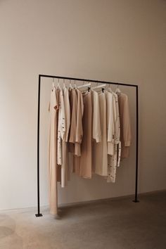 a rack with clothes hanging on it in front of a white wall and a black metal frame