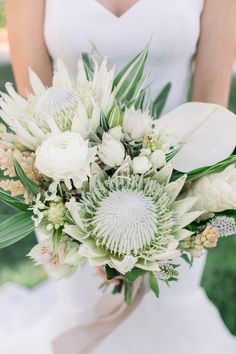 a bridal bouquet with white flowers and greenery is held by a woman in a wedding dress